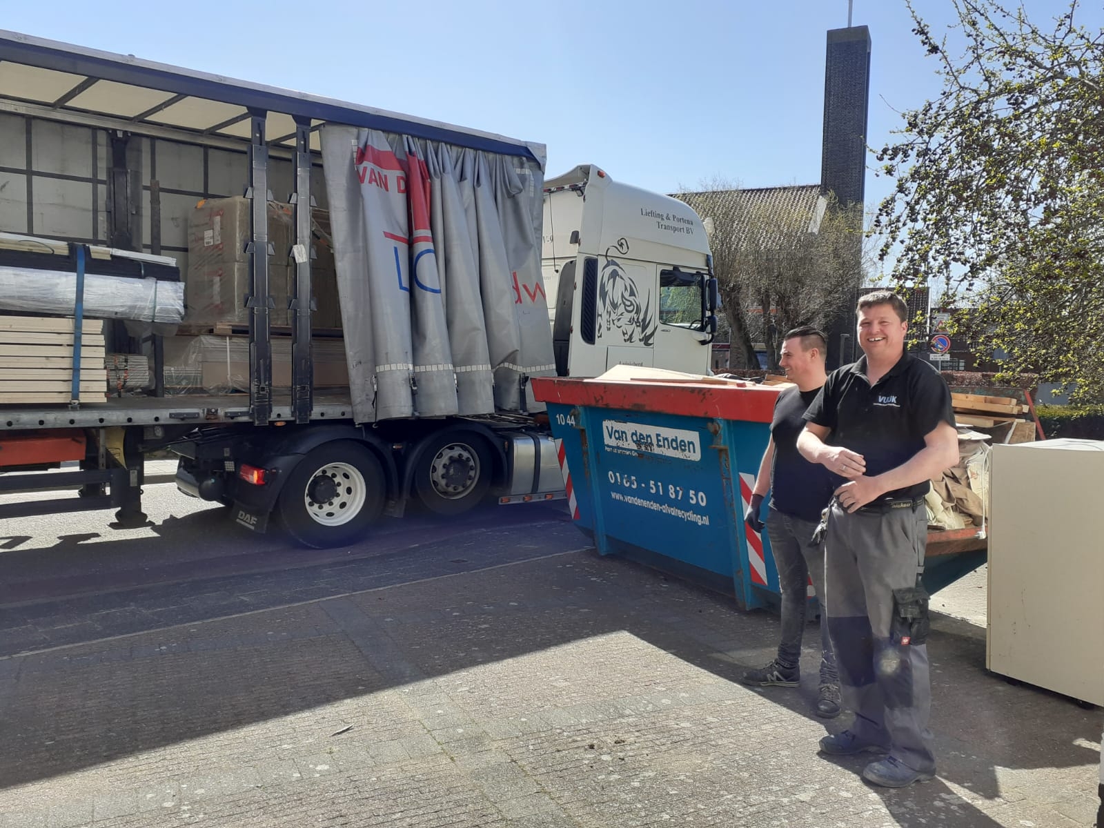 Twee mannen van Vuijk bij de aanlevering van materiaal: vrachtwagen met hout en een container