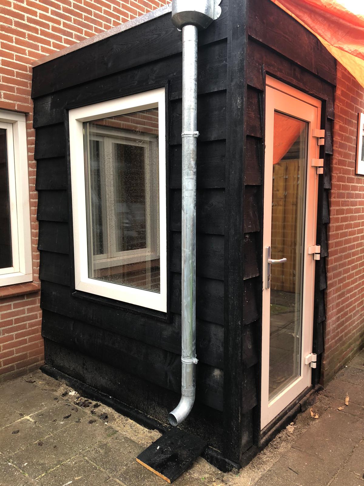 Aanbouw met zwarte houten rabatdelen, wit raam en witte deur